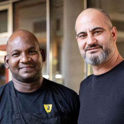 Zwei Männer in schwarzer Kleidung, einer davon trägt eine Schürze mit gelbem Logo.