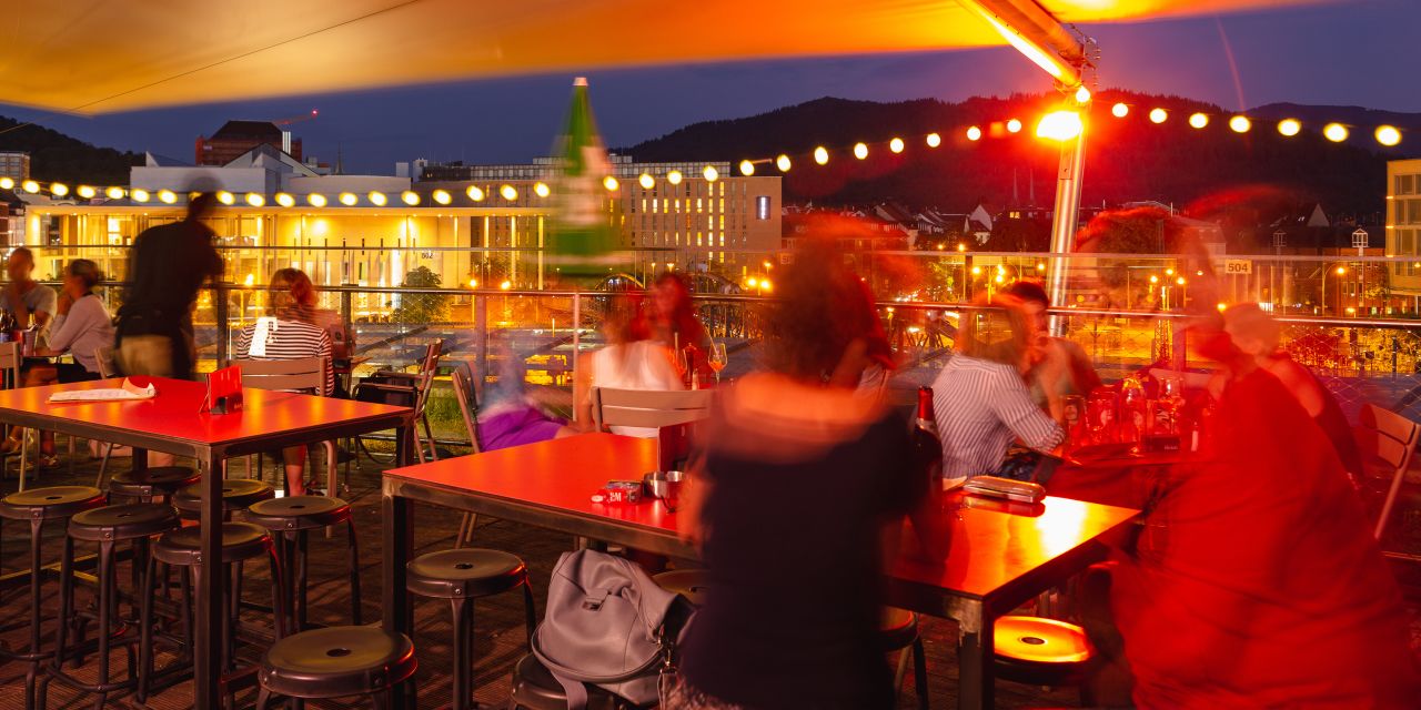 Gut besuchte Dachterasse am Abend, mit Blick auf die Stadtkulisse.